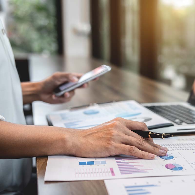 Accountant sitting at a desk, checking his phone and charts on the table