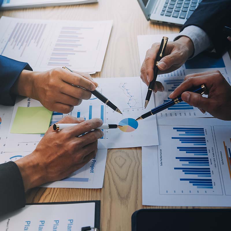 Colleagues around a desk pointing at charts with their pens.
