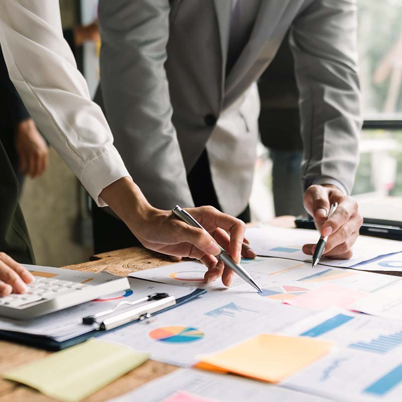 Accountants standing over a desk, pointing at charts